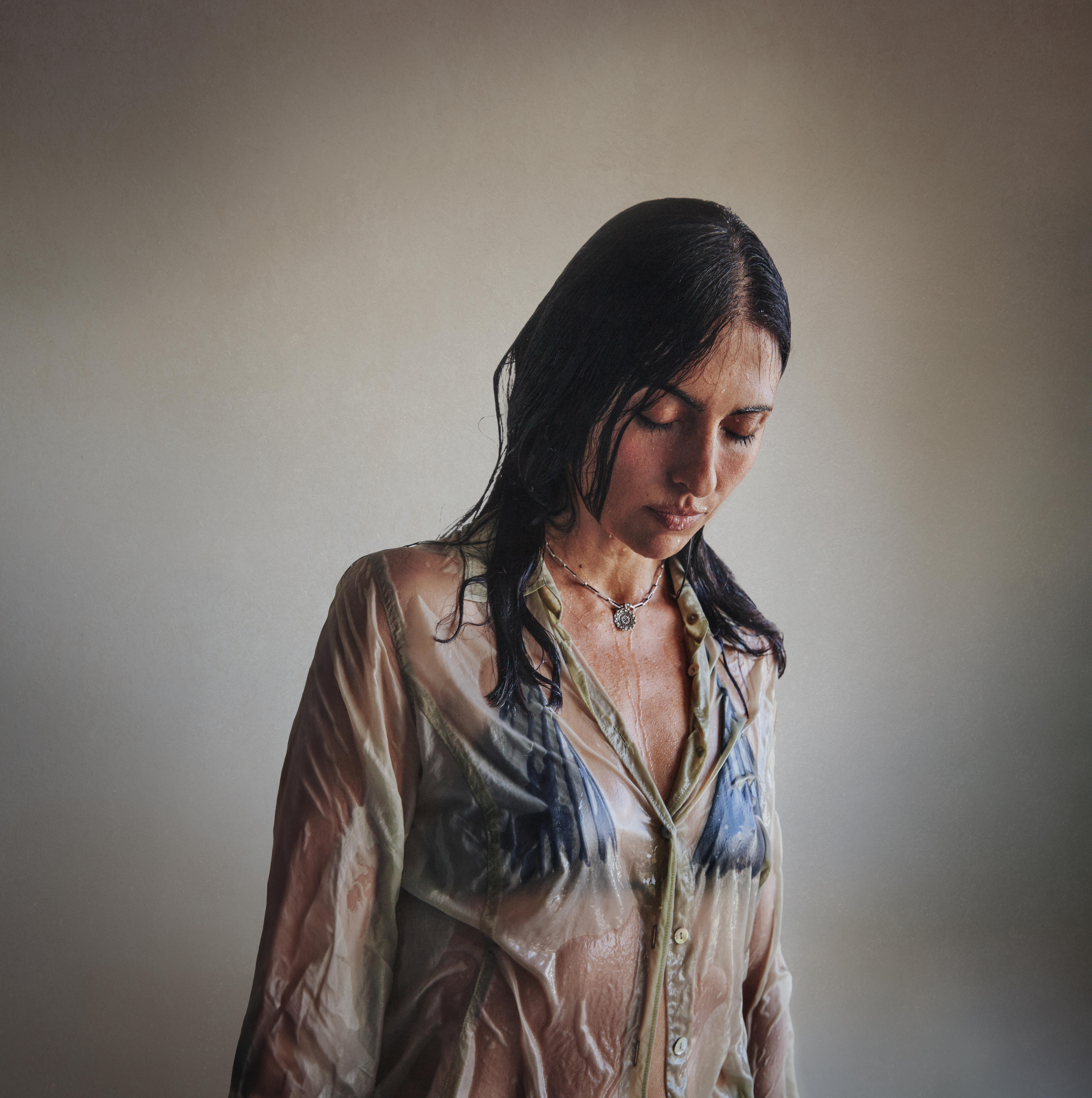A woman stands drenched wet looking down at the floor