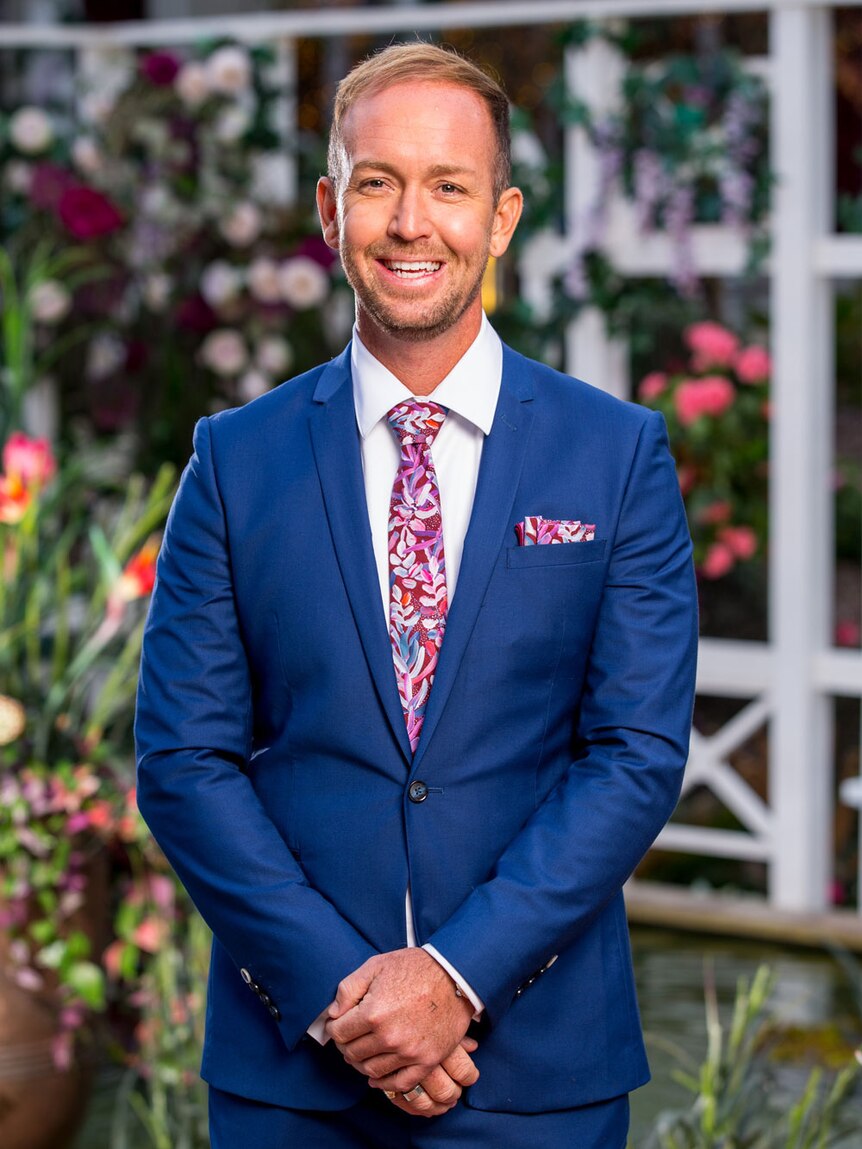 Promotional photo of Jess Glasgow smiling in a suit on The Bachelorette 2019 television program.