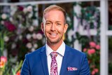 Promotional photo of Jess Glasgow smiling in a suit on The Bachelorette 2019 television program.