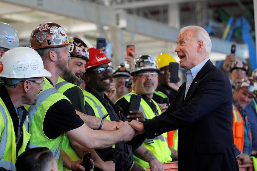 Joe Biden shaking hands with workers in hard hats and high vis vests