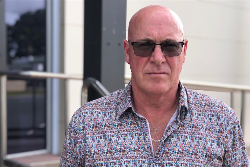 Man in colourful shirt and sunglasses looks to camera. 