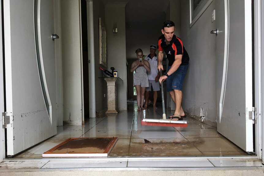Man sweeps mud out of his house in Townsville after floods.