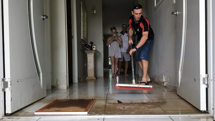 Man sweeps muddy water out of his house in Townsville after floods.