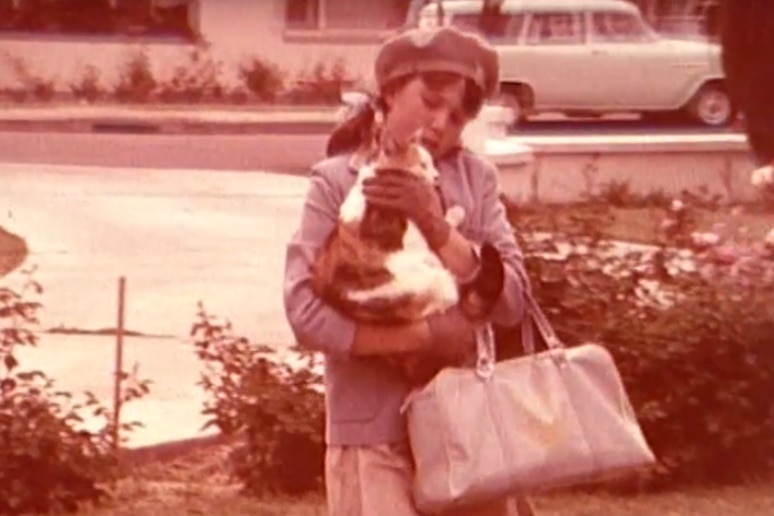 1960s photo of a girl in school uniform holding a cat and a large bag