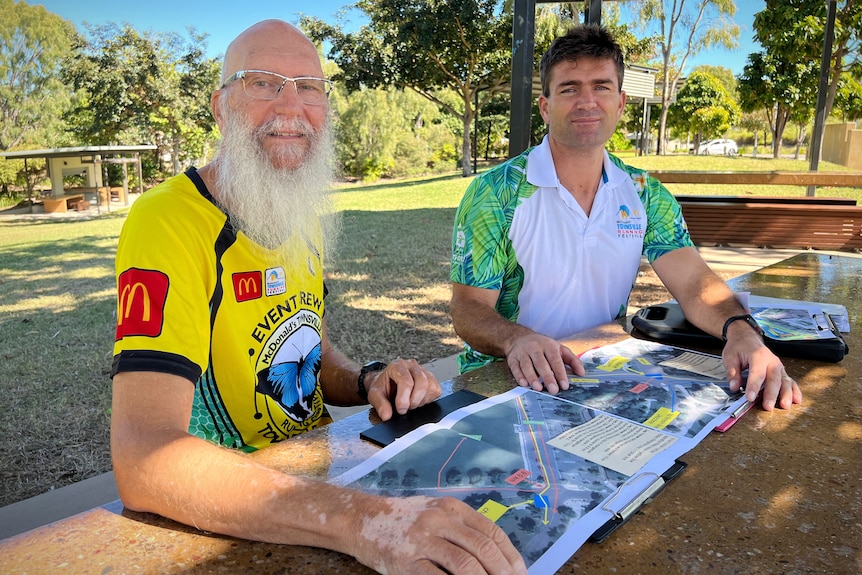 Two men sit at a park table with maps of a race course 