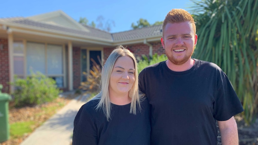 A young man and woman smiling outside a home