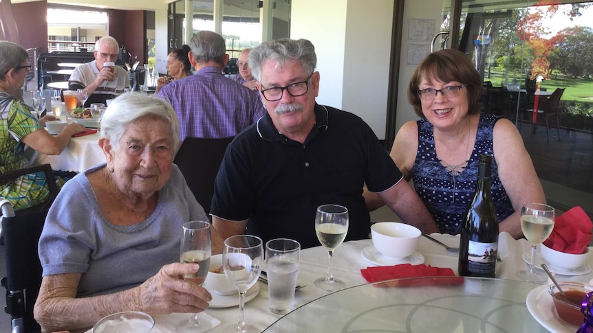 Norma Newlyn, holding a glass of wine, sitting at an outside cafe table with her son Greg and daughter-in-law Gloria