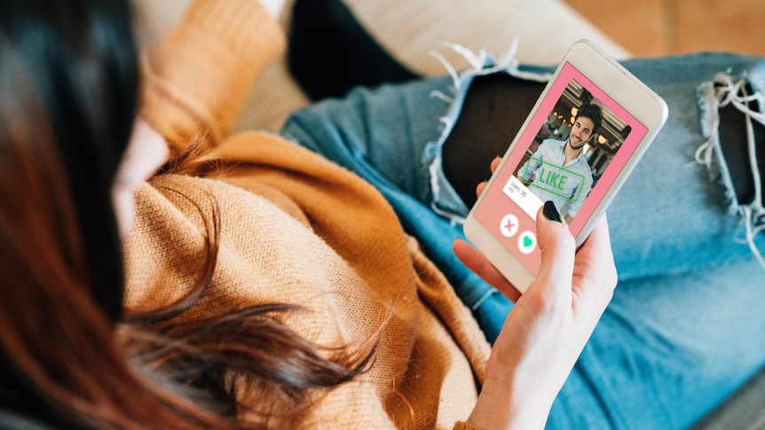 back of head shot of woman with phone in her hand and dating app open with a photo of a man and the word 'like' across it