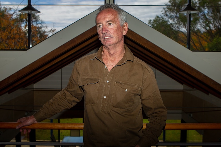 A man stands in front of large windows.