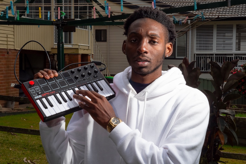 Music producer Egrinya Adie pictured in his backyard near the clothesline holding a music keyboard