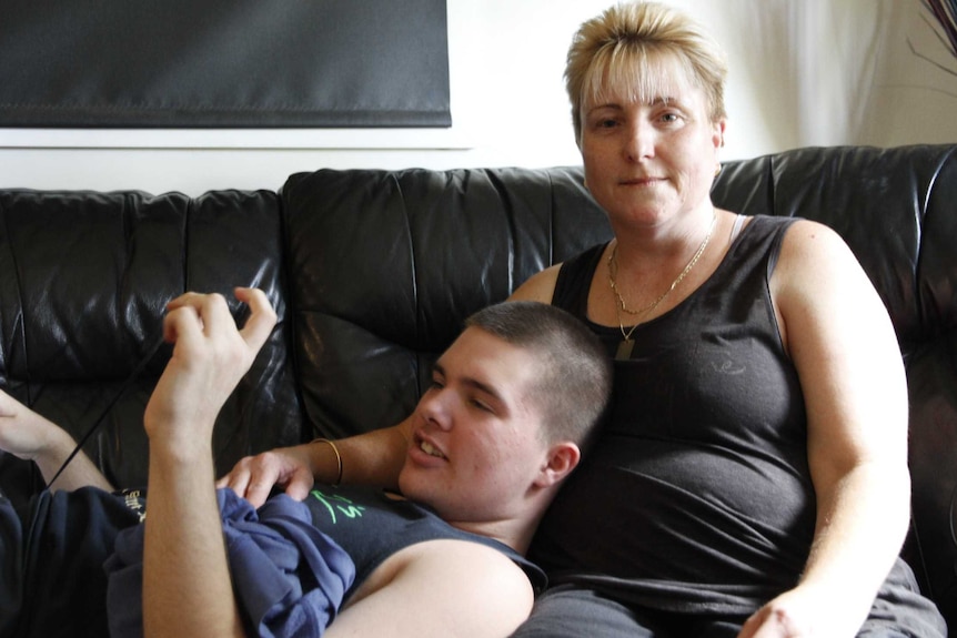 A woman sits on a sofa with her son leaning up against her.