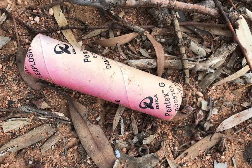 A red tube with black writing on it on the ground in bushland in Western Australia.