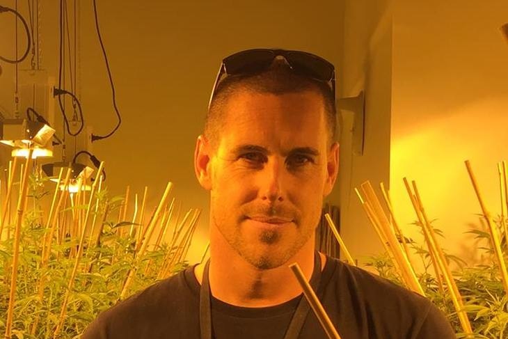 A man standing in the middle of marijuana greenhouse, with plants on either side of him.