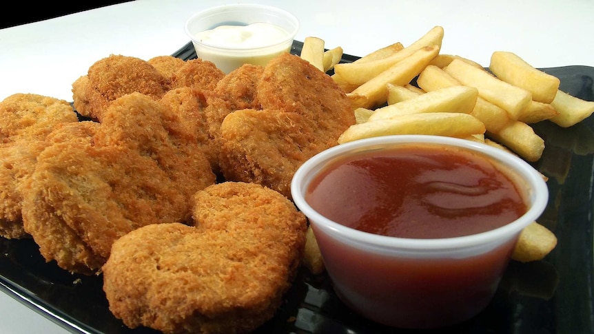 Chicken nuggets and chips on a plate with aioli and tomato sauce.