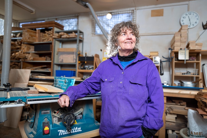 A middle-age woman smiling while standing in the woodwork shed.