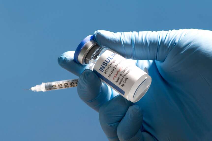 A gloved hand holding a vial of insulin and a syringe.