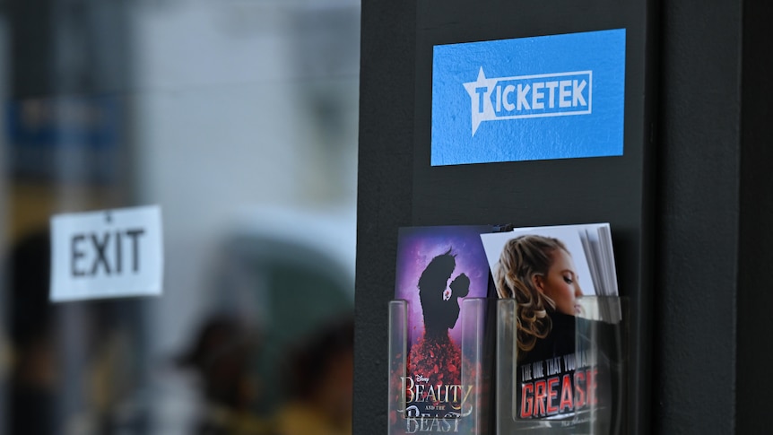 A blue Ticketek sign above a pair of pamphlets on a wall.