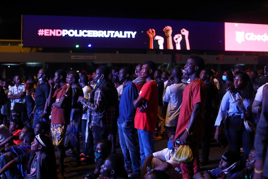 Men stand in dark illuminated by sign which reads '#endpolicebrutality'