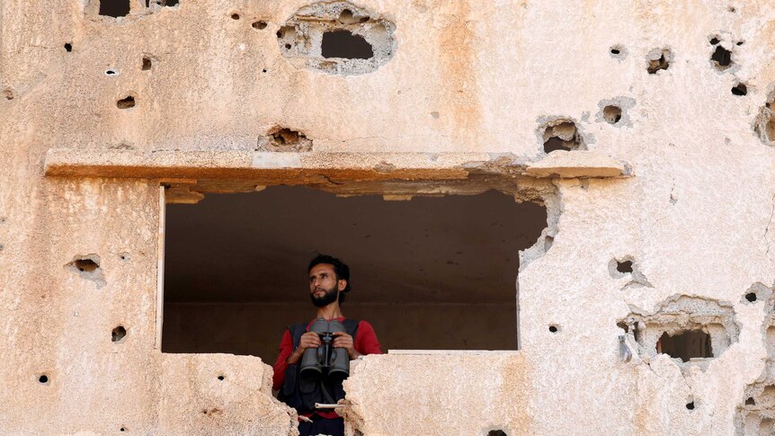 A Free Syrian Army fighter looks through a hole in a bullet punchered wall in Yadouda, Daraa