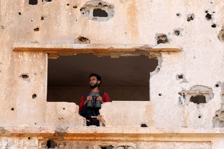 A Free Syrian Army fighter looks through a hole in a bullet punchered wall in Yadouda, Daraa