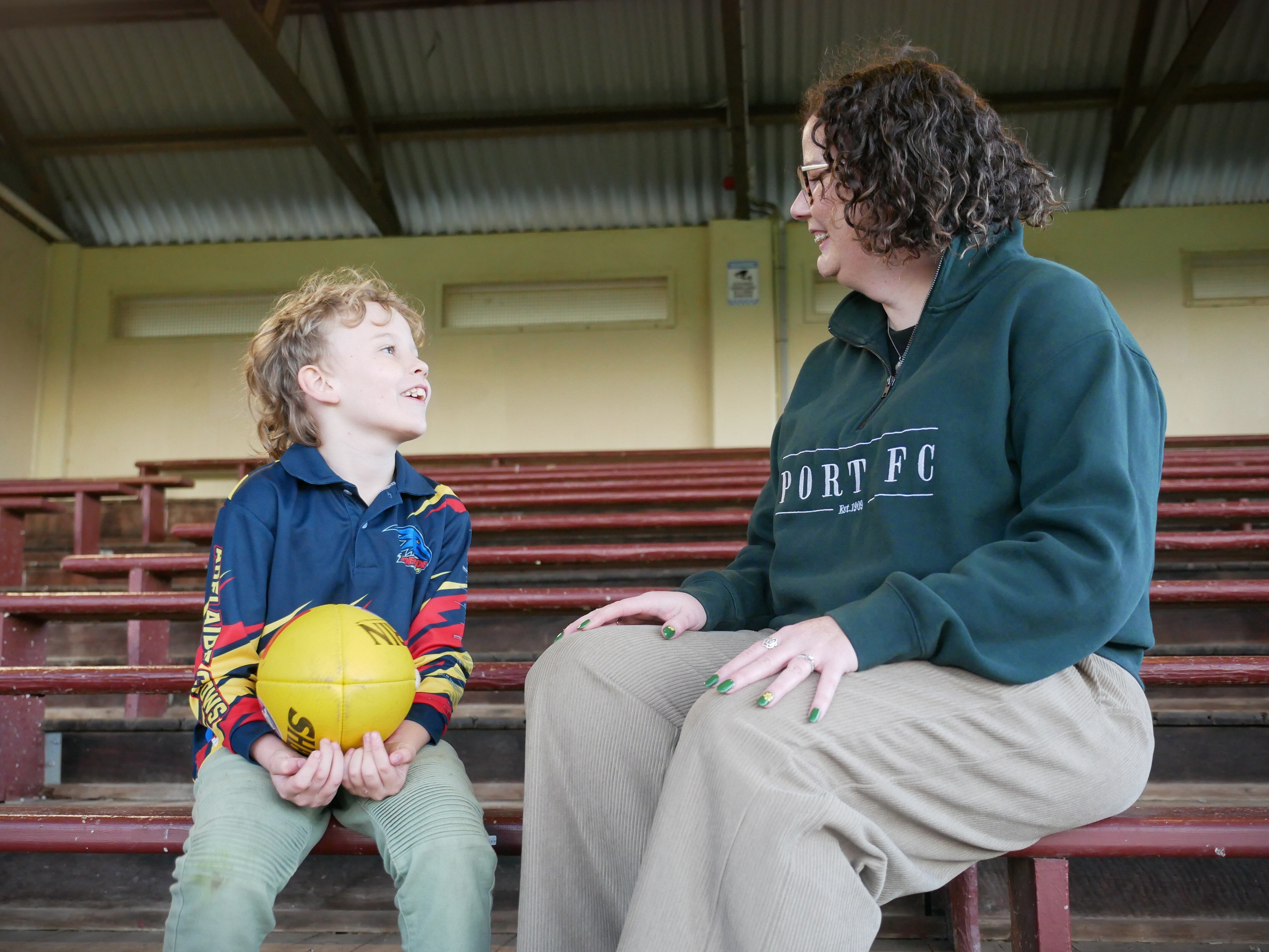 A mother and a young boy holding a football look at each other sitting in oval stands