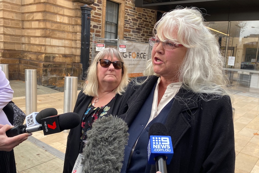 A woman speaks in front of the media microphones