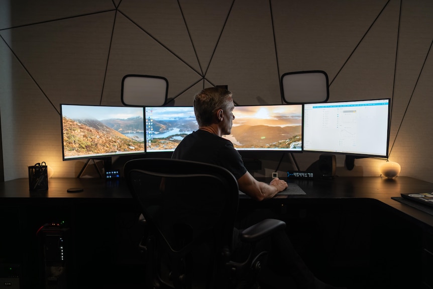 A man typing on a computer with multiple screens curved around him