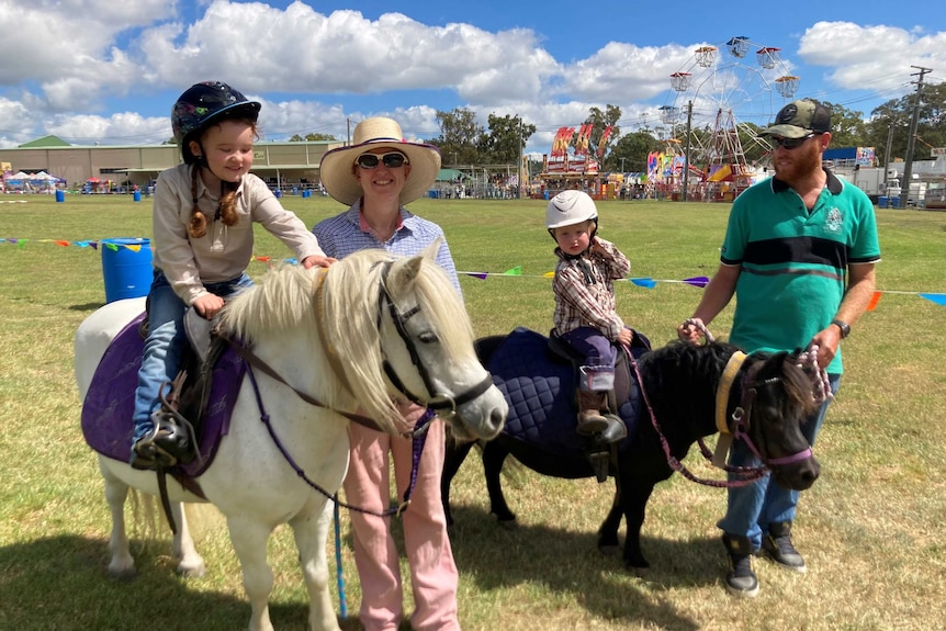 Two small children sit on their ponies while their mother and father hold the reins.