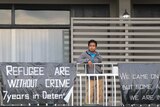 Abdul Sattar, standing on the balcony of the Kangaroo Point Central Hotel and Apartments, next to defiant signs made on bin bags