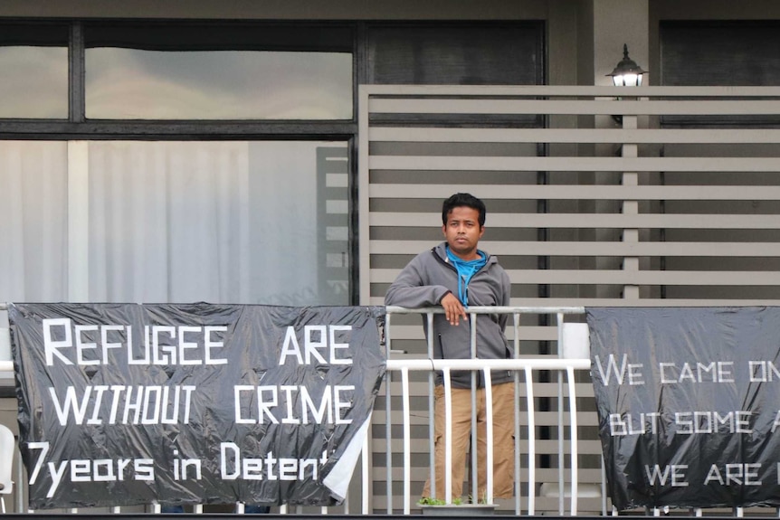 Abdul Sattar, standing on the balcony of the Kangaroo Point Central Hotel and Apartments, next to defiant signs made on bin bags