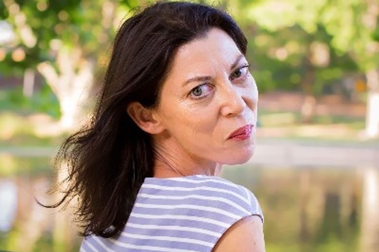 Alison Evans looks over her shoulder and smiles slightly in a park setting