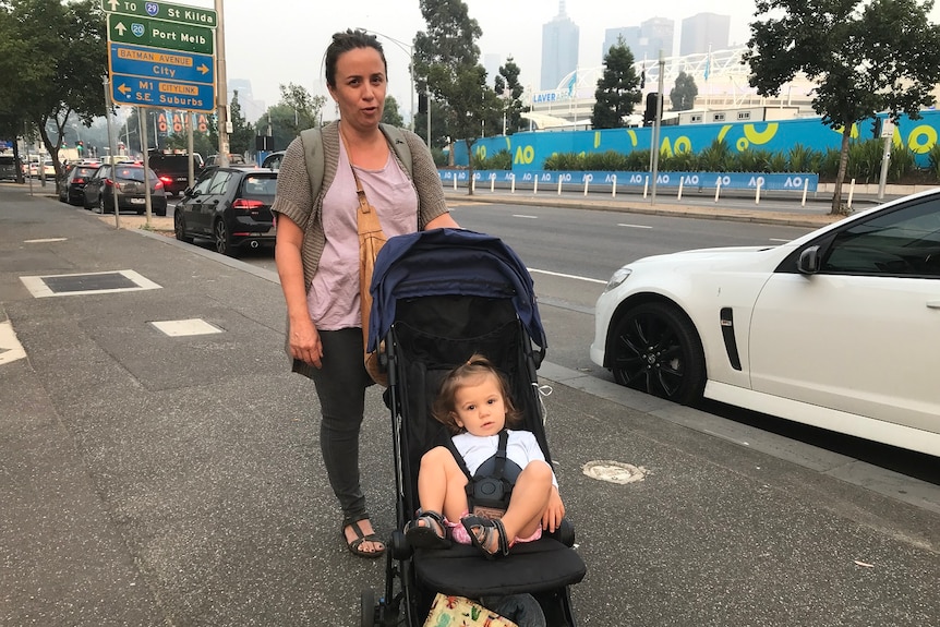 Juliana Pedrosa stands behind a pram with her 17-month-old daughter inside, under a smoky sky outside Melbourne Park.