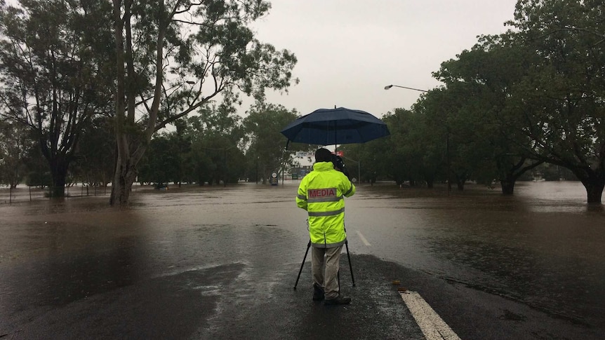 An ABC cameraan stands at the edge of floodwater in Lismore