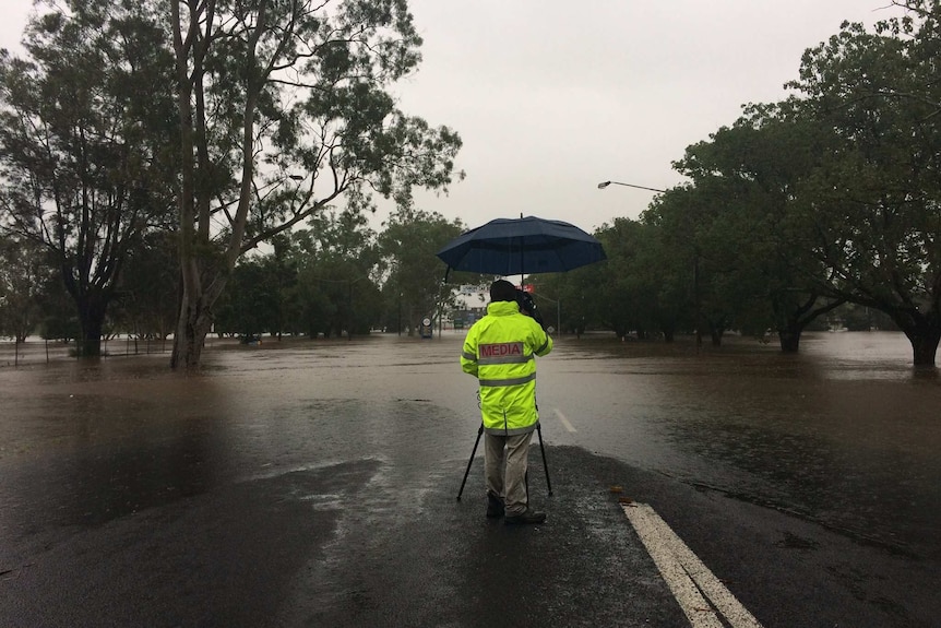 An ABC cameraan stands at the edge of floodwater in Lismore