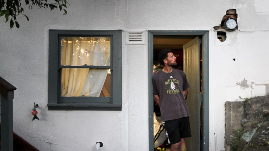 Sydney resident Damian James stands in the doorway to a storeroom and looks at asbestos in the wall.