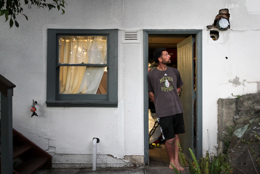 Sydney resident Damian James stands in the doorway to a storeroom and looks at asbestos in the wall.