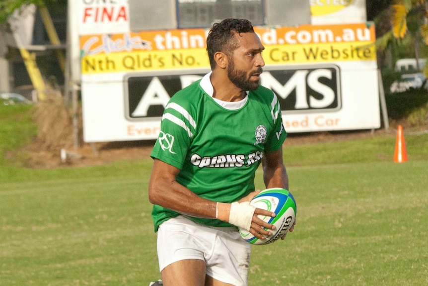 A man wearing a green jersey holding a rugby ball.