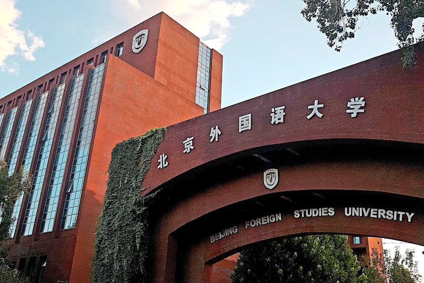 A red brick arch partially covered in hanging, leafy plants leading to the Beijing Foreign Studies University's West Campus.