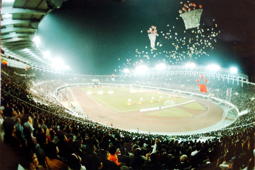 A view of a packed stadium for an opening ceremony of a football tournament, with ballons floating above ground. 