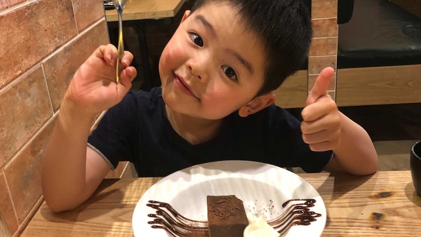 A young boy poses in a restaurant with a piece of chocolate cake.