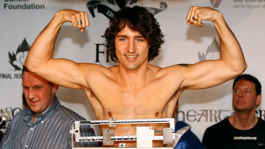 A shirtless Justin Trudeau on a set of scales flexes his muscles 