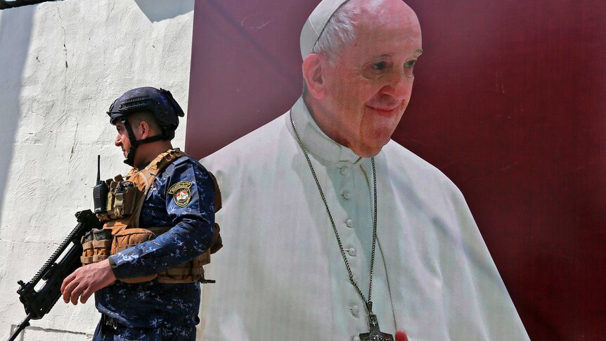 A member of the Iraqi forces stands next to a poster depicting an image of Pope Francis at the Syriac Catholic Church.