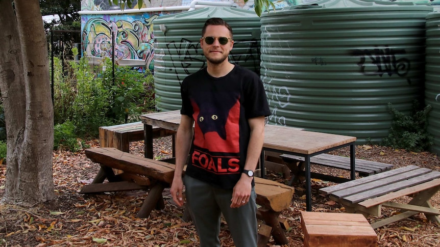 Chris Harold standing in an outdoor area next to a wooden bench and trees.