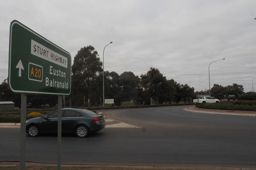 A car travelling through a roundabout with a road sign for the Sturt Highway in the foreground.