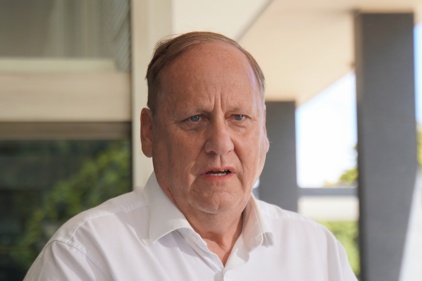 A man in a white collared shirt looks serious. 