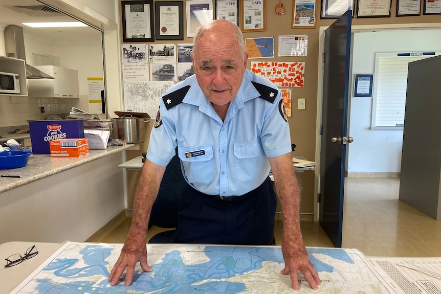 A man in  a blue SES uniform leans over a flood map.