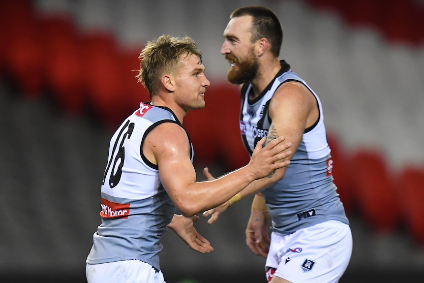 Two Port Adelaide AFL players shake hands as they celebrate a goal against St Kilda.
