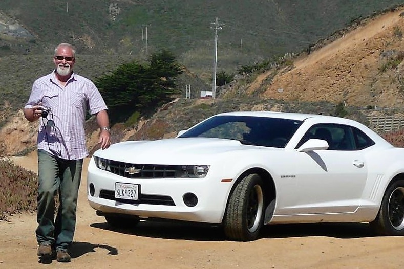 A man holding a camera walking away from a white Mustang.