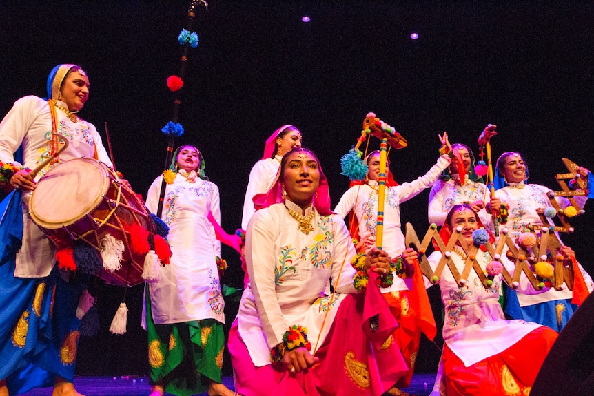A bunch of musicians wear colourful Indian clothes on a stage