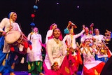 A bunch of musicians wear colourful Indian clothes on a stage